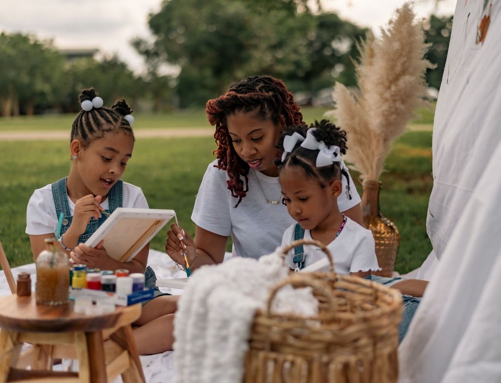 Loved ones enjoy reading books together while having a picnic outdoors with drinks and snacks on a sunny day.