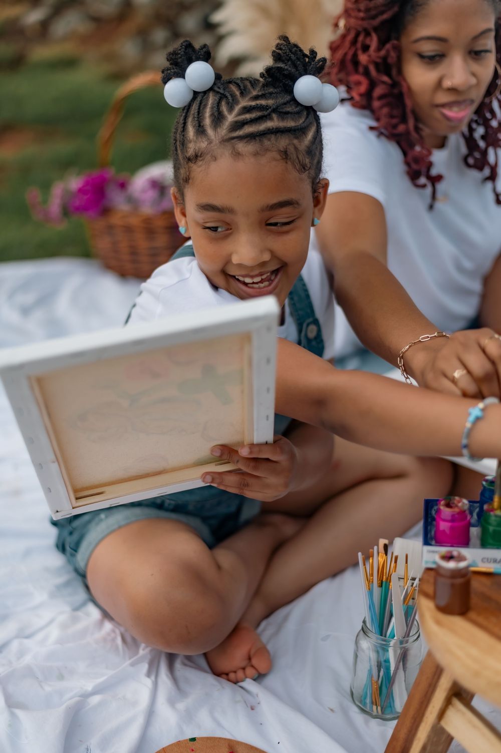 Young child enjoying art time with colorful art supplies on a white blanket during outdoor picnic setting.