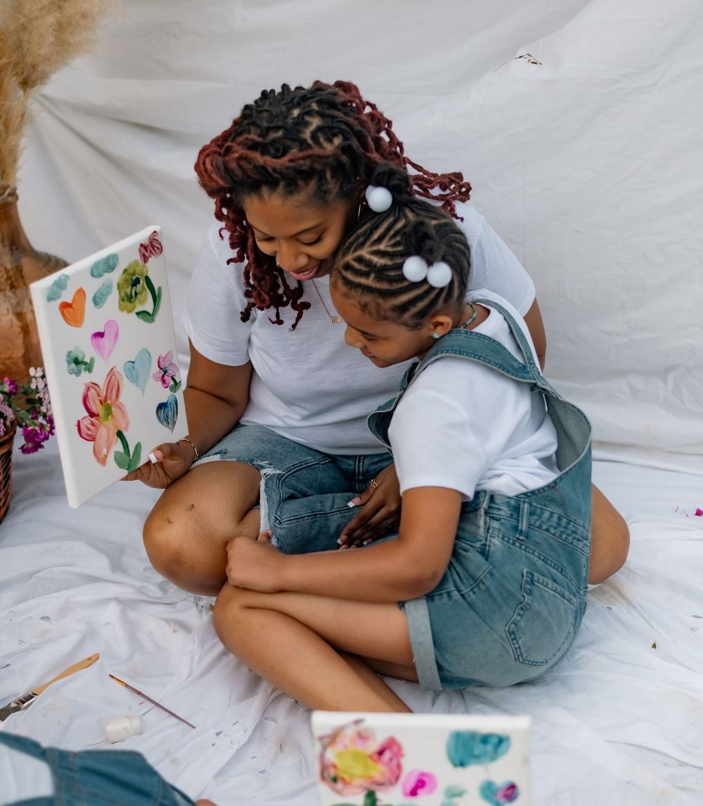 Someone in a white shirt and denim sits on a white surface with watercolor supplies and paper for painting.