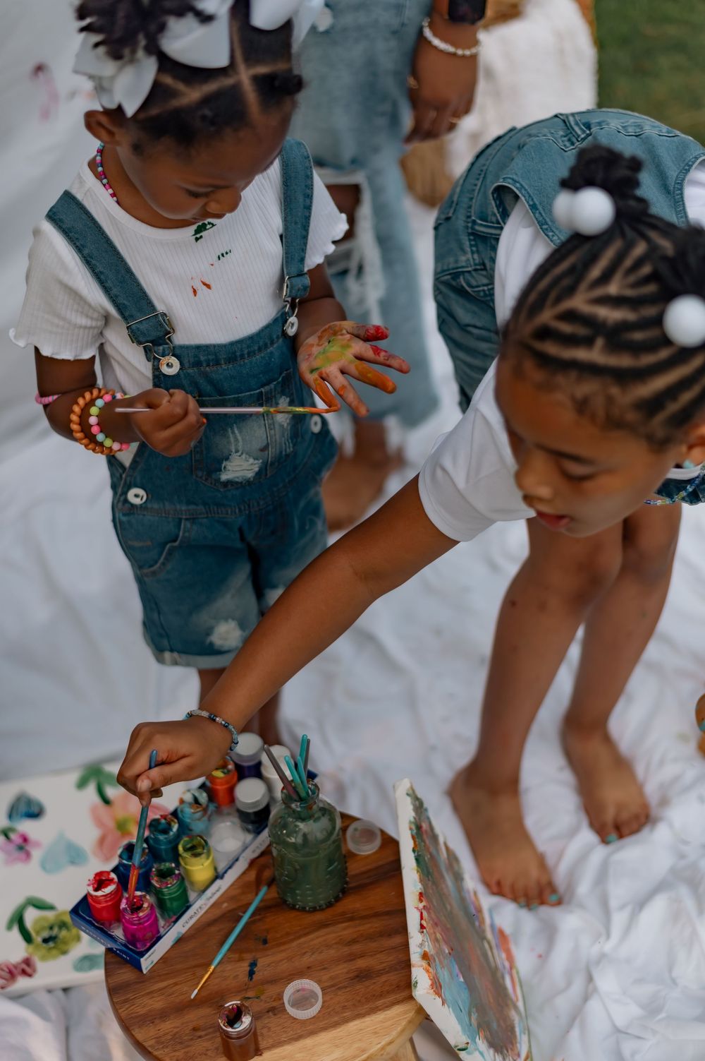 Young children engage in creative painting activities on a wooden surface with colorful art supplies and cotton balls.