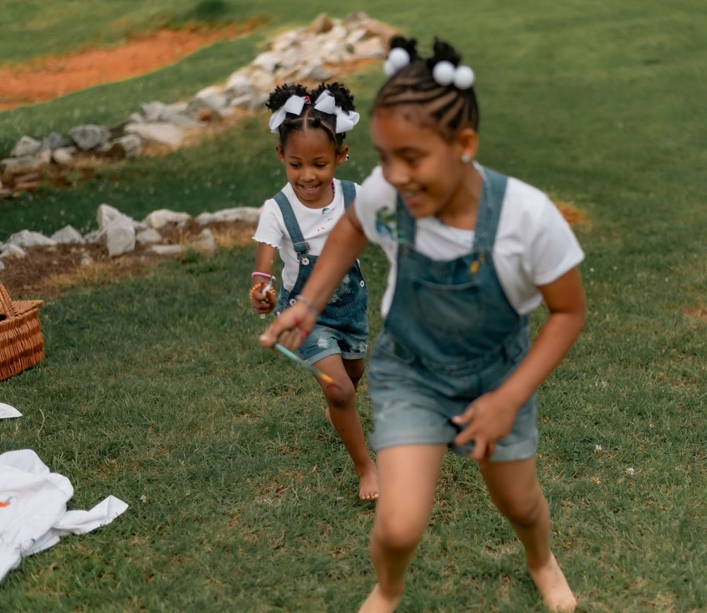 Two young children in denim outfits play together on a grassy lawn on a sunny summer day.