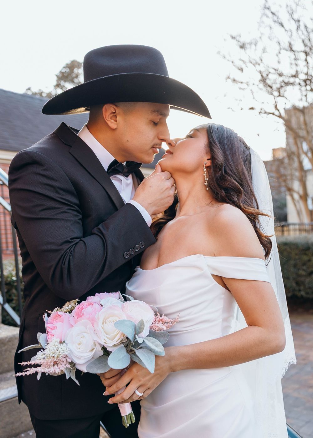 A tender wedding moment with pink and blue floral bouquet against a brick building backdrop. North Carolina wedding.