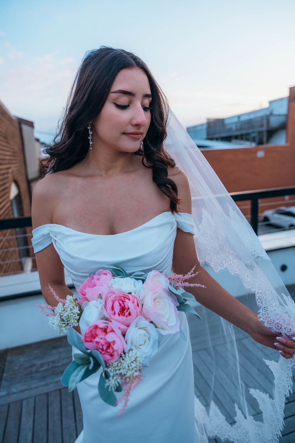 A bride in white dress holds a pink and white bouquet on a rooftop setting. North Carolina.