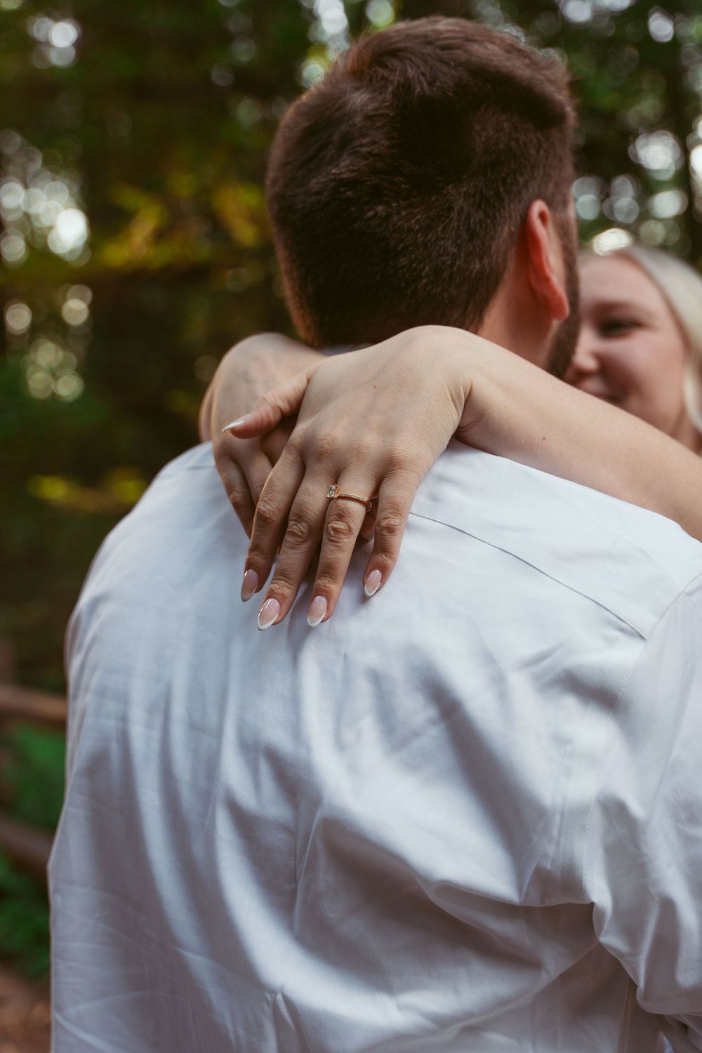 Close-up shots showing hands with rings embracing across someone wearing a white shirt against a natural background.
