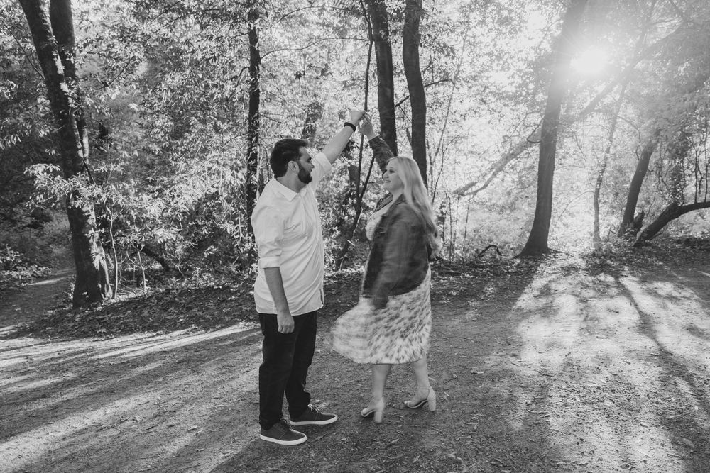 Silhouetted figures walk along a sunlit forest path as sunbeams filter through trees creating a dreamy atmosphere.