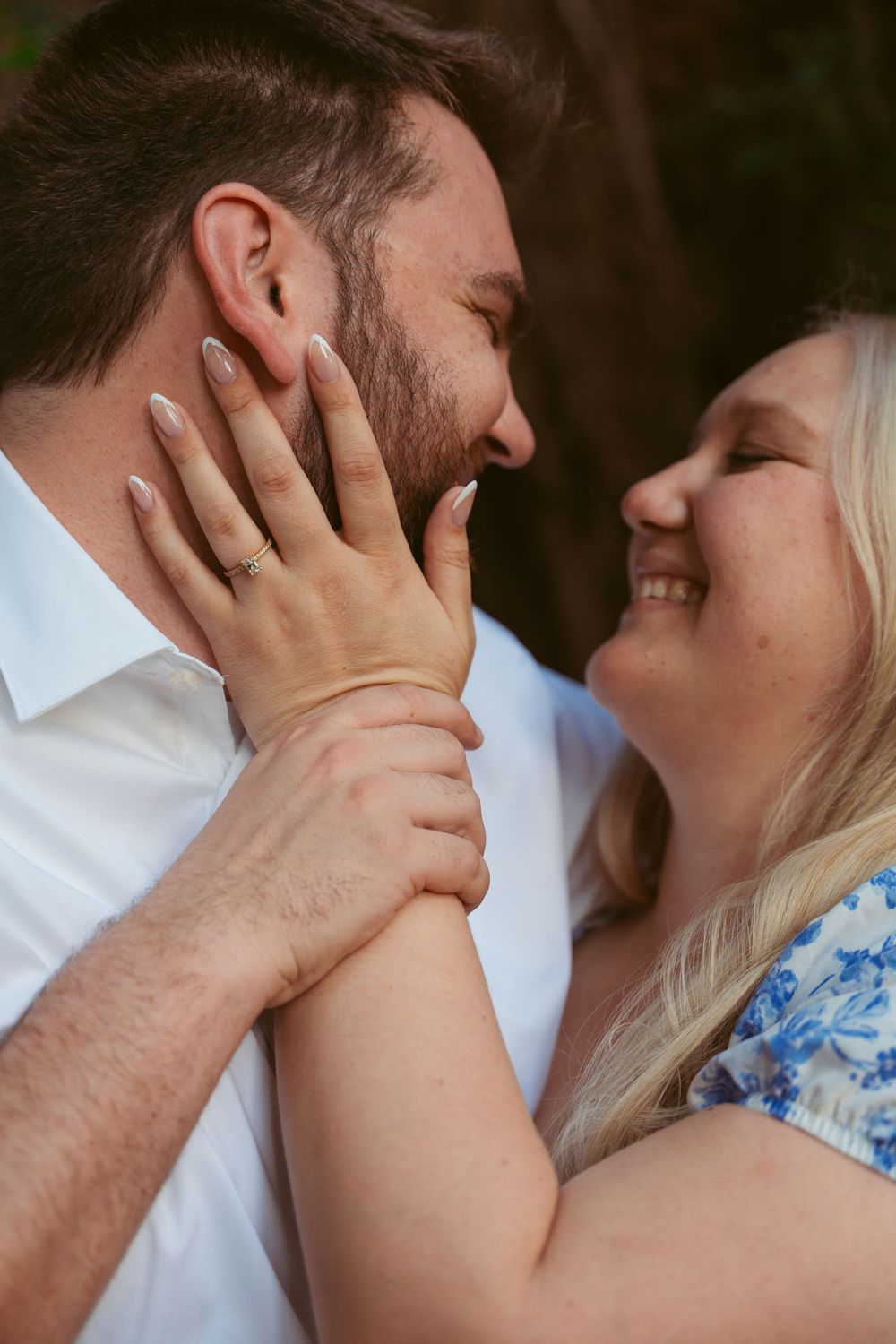 Close up romantic moment between a couple in a white shirt and blue floral dress sharing a tender kiss outdoors.
