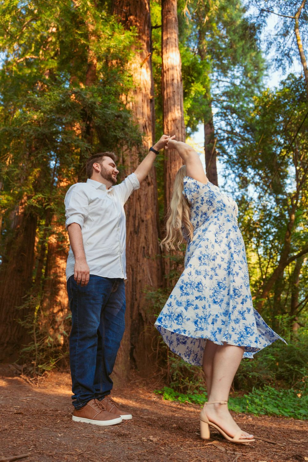 Romantic photo series of a couple posing playfully against redwood trees in a sunlit forest setting.