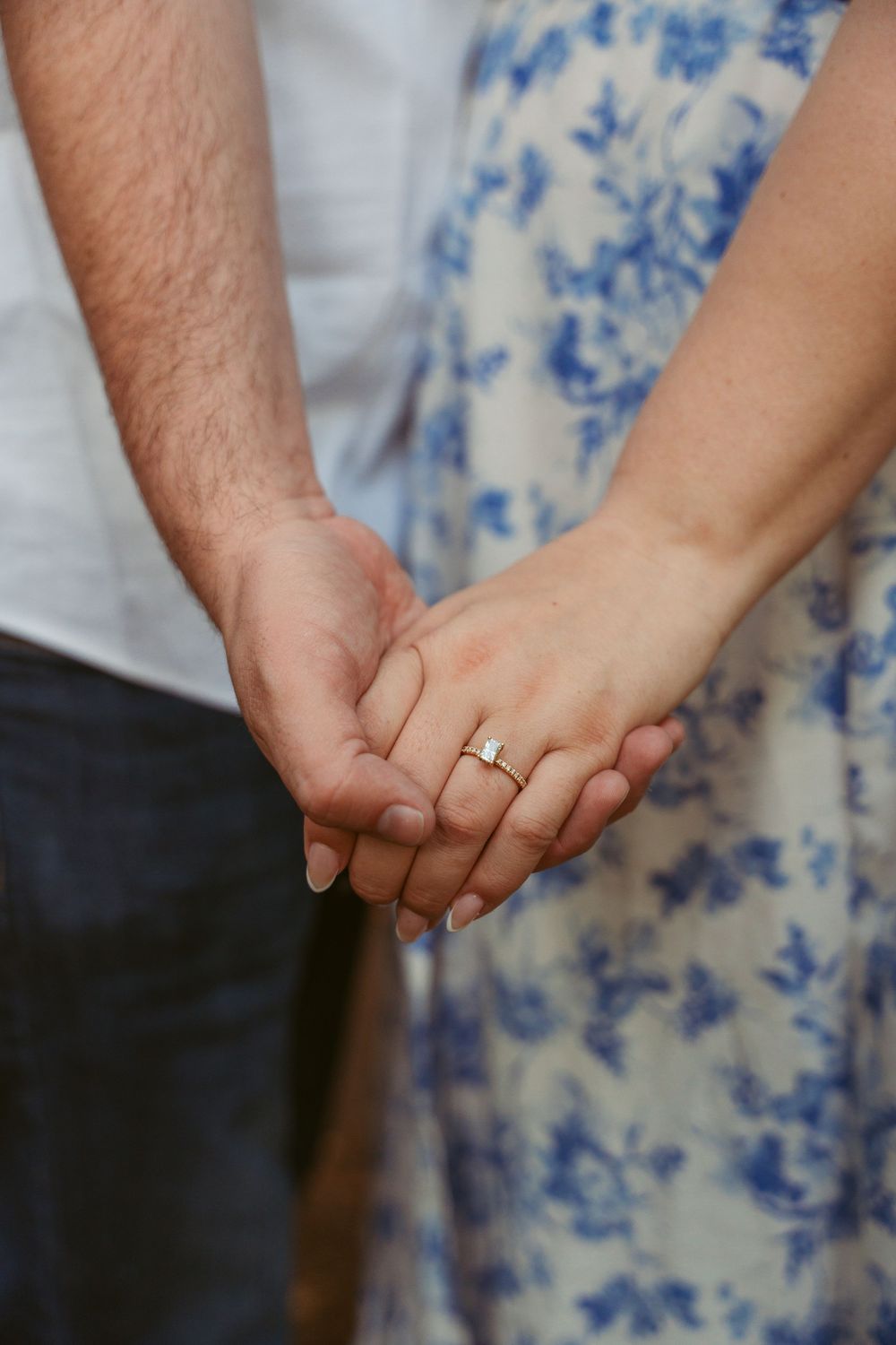 Close-up of hands with an engagement ring, with a white and blue floral dress in the background.