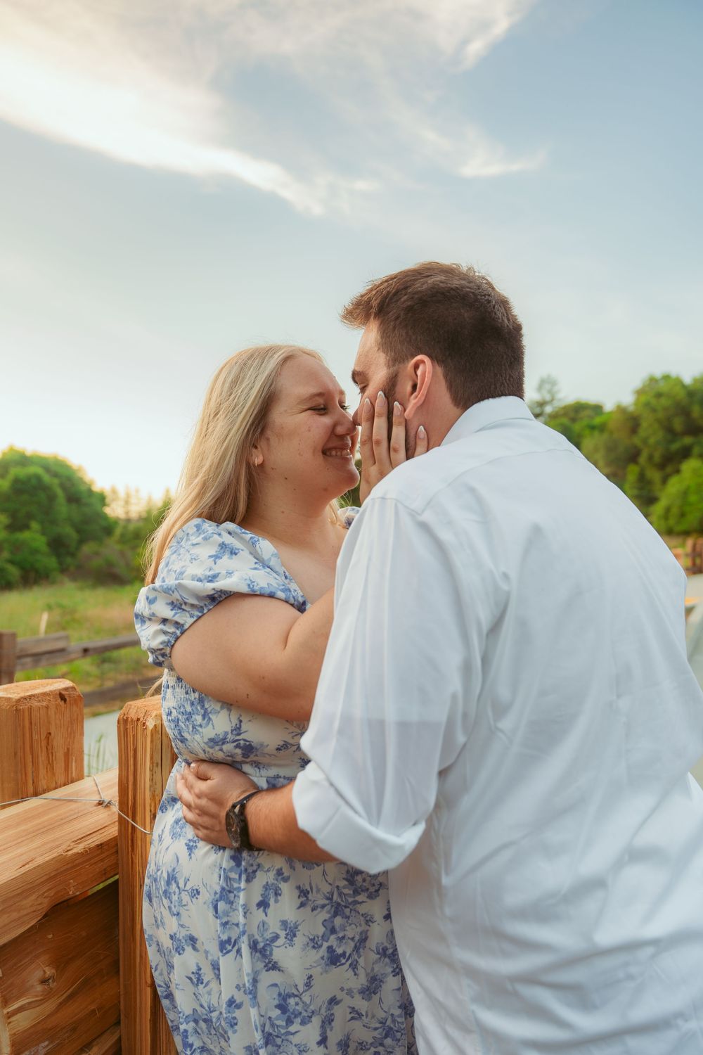 Romantic couple sharing an intimate moment on a wooden deck during sunset with trees in the background.