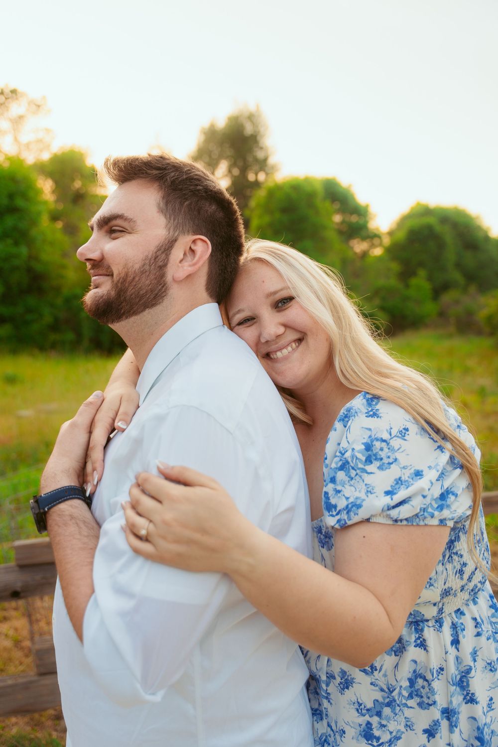 A couple shares a tender embrace in an outdoor setting during golden hour, wearing white and blue floral attire.