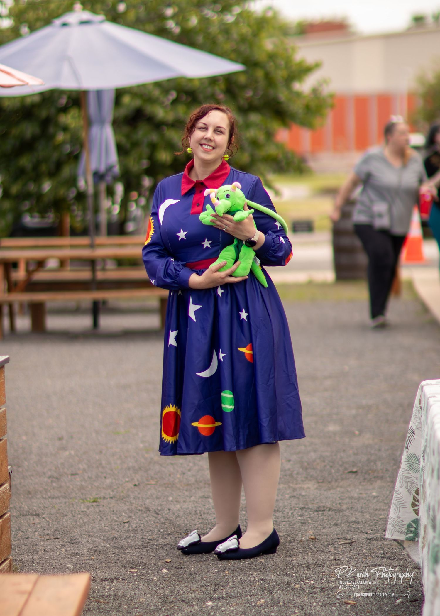 A figure in a navy blue dress with moon and star patterns stands next to a white bench in an outdoor setting.