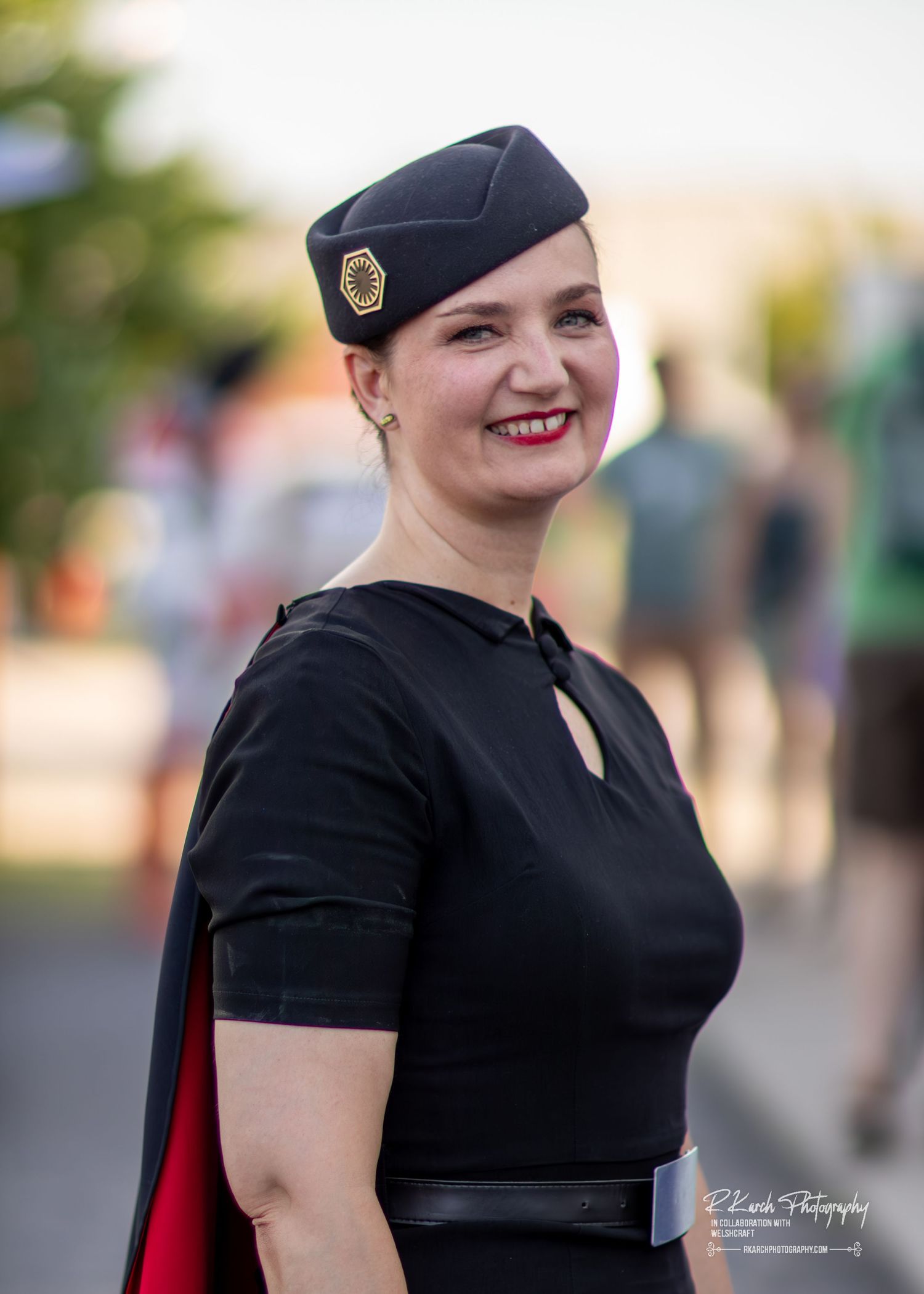 A person wearing a black beret and matching short-sleeved top poses outdoors at an event.