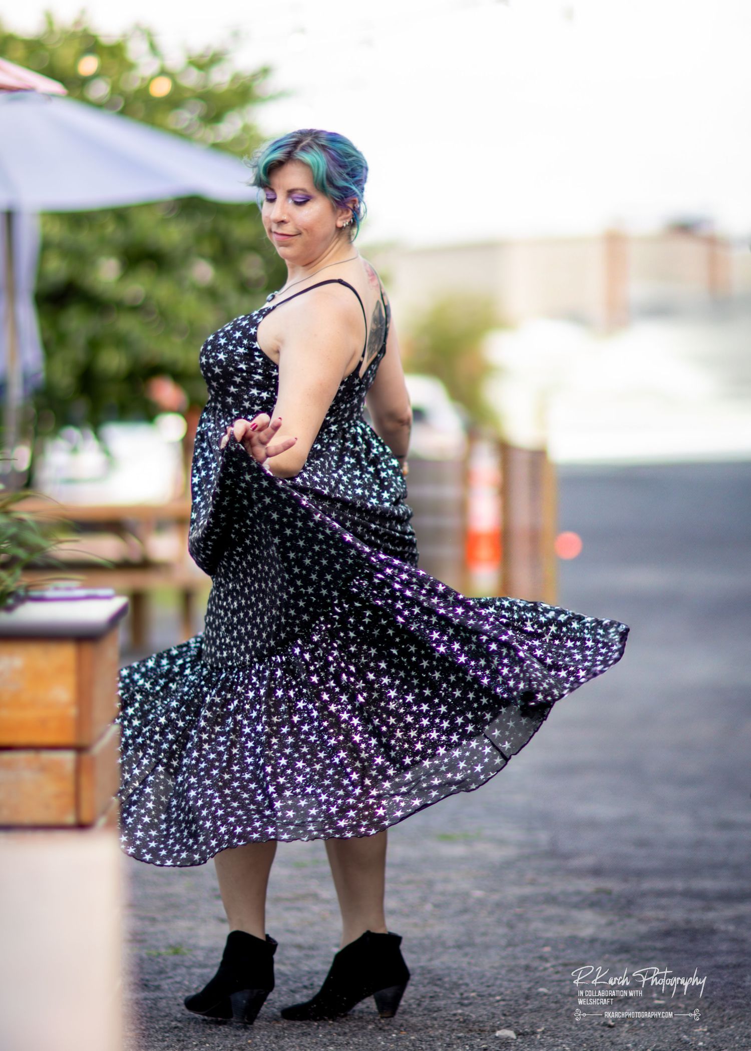 A polka dot dress twirls gracefully in an outdoor setting with black ankle boots and blue-tinted hair.