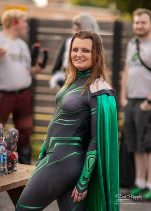 Person wearing green superhero costume with matching cape poses at outdoor event.