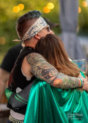 A couple embraces at an outdoor event, showcasing colorful tattoo sleeves and a green satin dress.