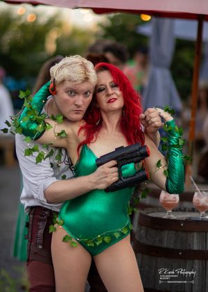 Cosplay scene with performers in green costumes holding prop weapons in dramatic pose.