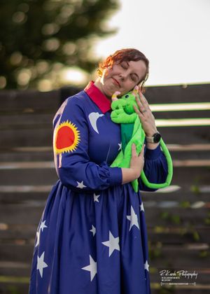 Person in starry navy dress holding a green plush toy at an outdoor gathering.