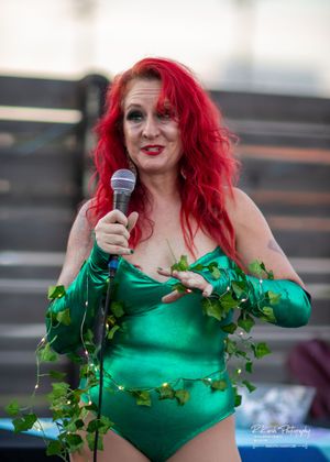 Performer in green costume with ivy decorations holds microphone during outdoor show.