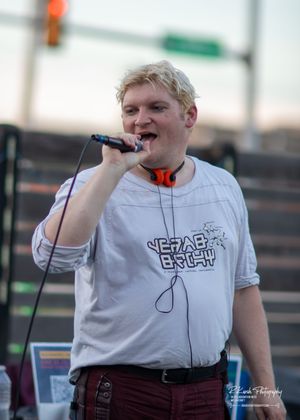 Performer in white t-shirt singing into microphone during outdoor concert performance.