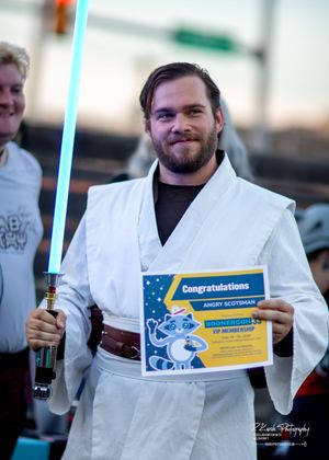 A person in white Jedi robes holds a blue lightsaber and a congratulations certificate with a winning smile.