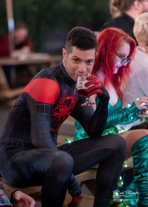 Person wearing Spider-Man costume sips from a wine glass at a themed party event.