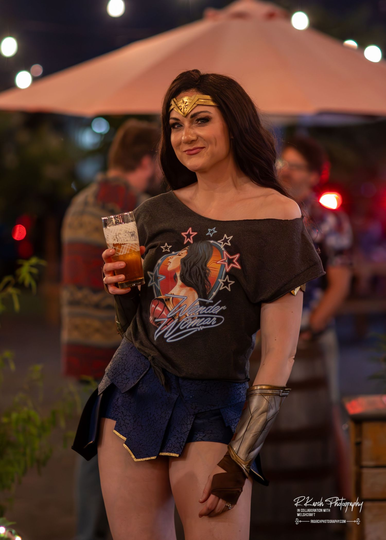 Wonder Woman cosplayer in casual outfit holding beverage at outdoor festival.