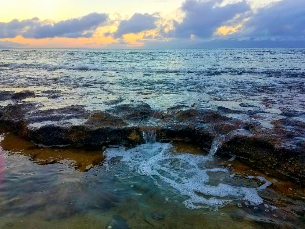 Dramatic sunset over rocky coastal waters with waves crashing against the shore.