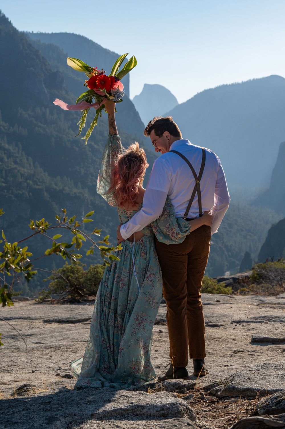 Couple celebrating with raised bouquet against dramatic Yosemite Valley backdrop.