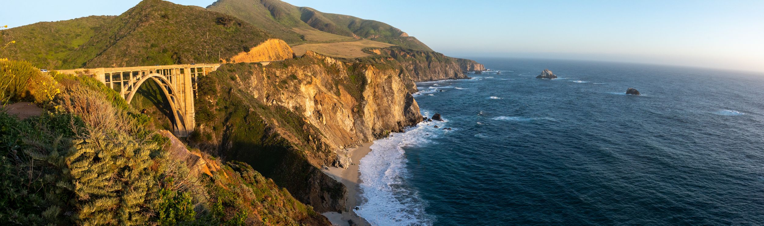 Panoramic view of Bixby Bridge along the Big Sur coastline with dramatic cliffs and ocean waves.