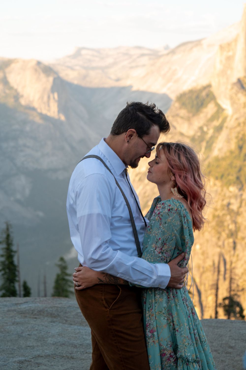Romantic couple embracing at sunset with Yosemite Valley mountains in background.