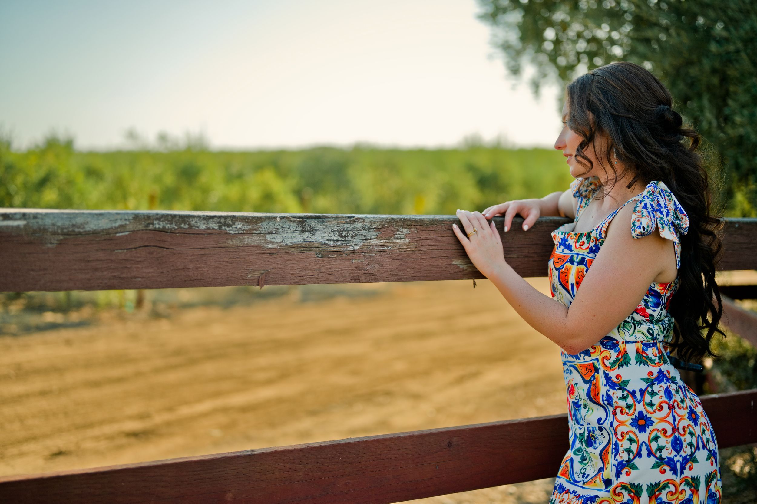Woman in floral dress looking out over scenic countryside from wooden railing.