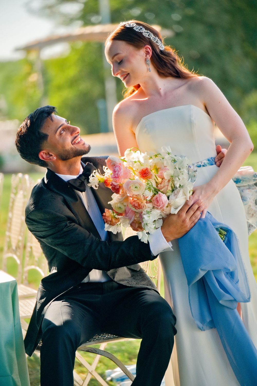 Joyful wedding couple sharing a romantic moment with colorful bouquet in an outdoor garden setting.