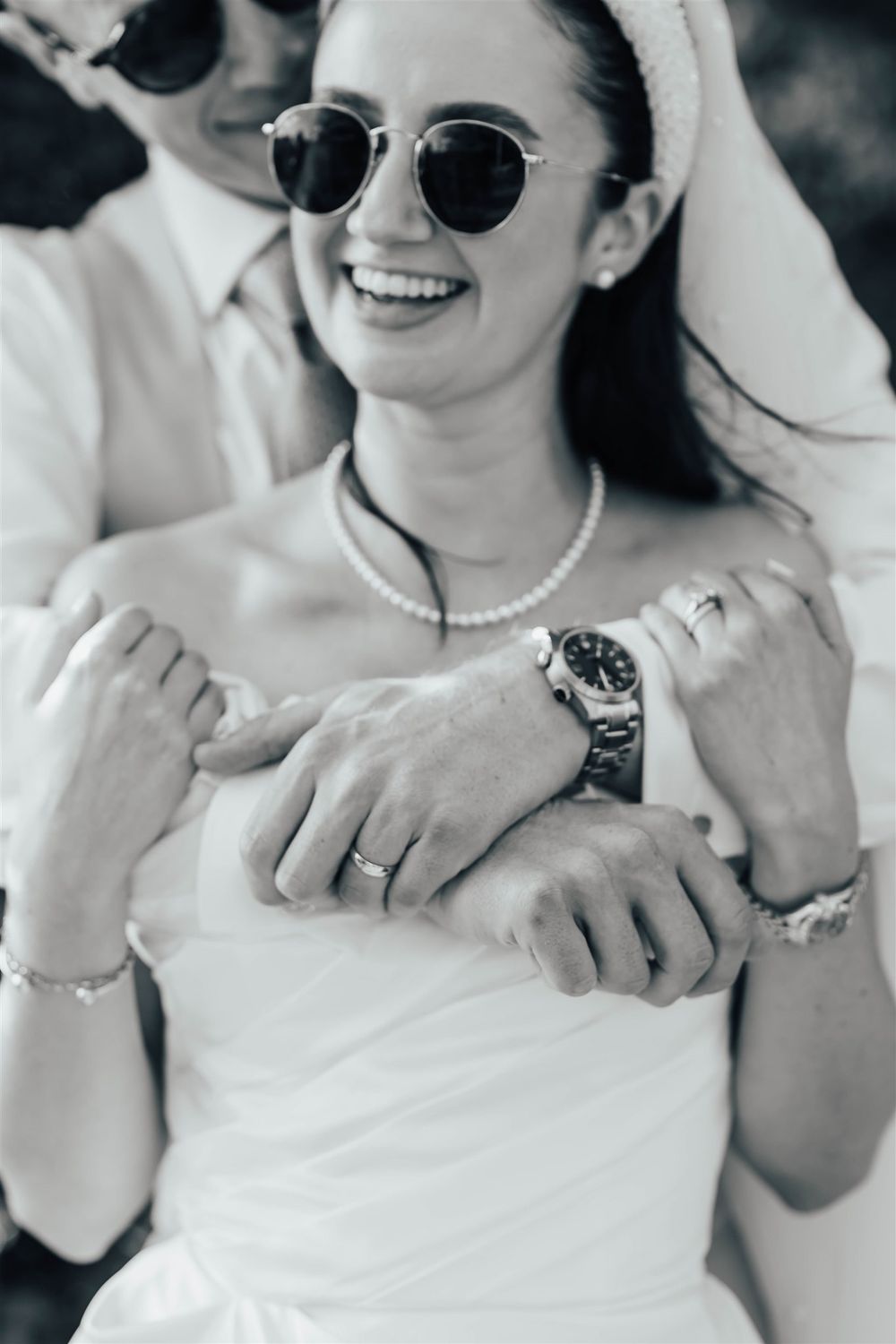 Black and white photo of a couple in wedding attire showing hands with rings, focused on intimate gestures and jewelry.