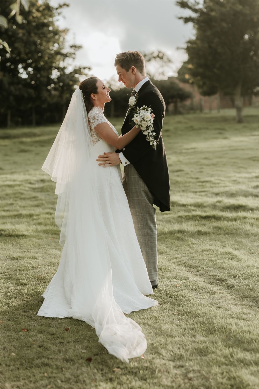 A romantic wedding photograph showing a couple embracing outdoors at sunset on a grassy lawn in North Yorkshire.