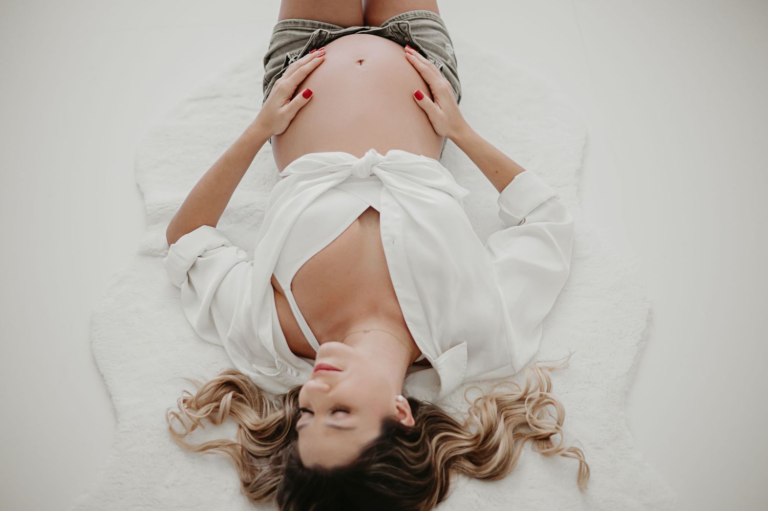 Artistic overhead maternity photo with flowing white fabric against light background.