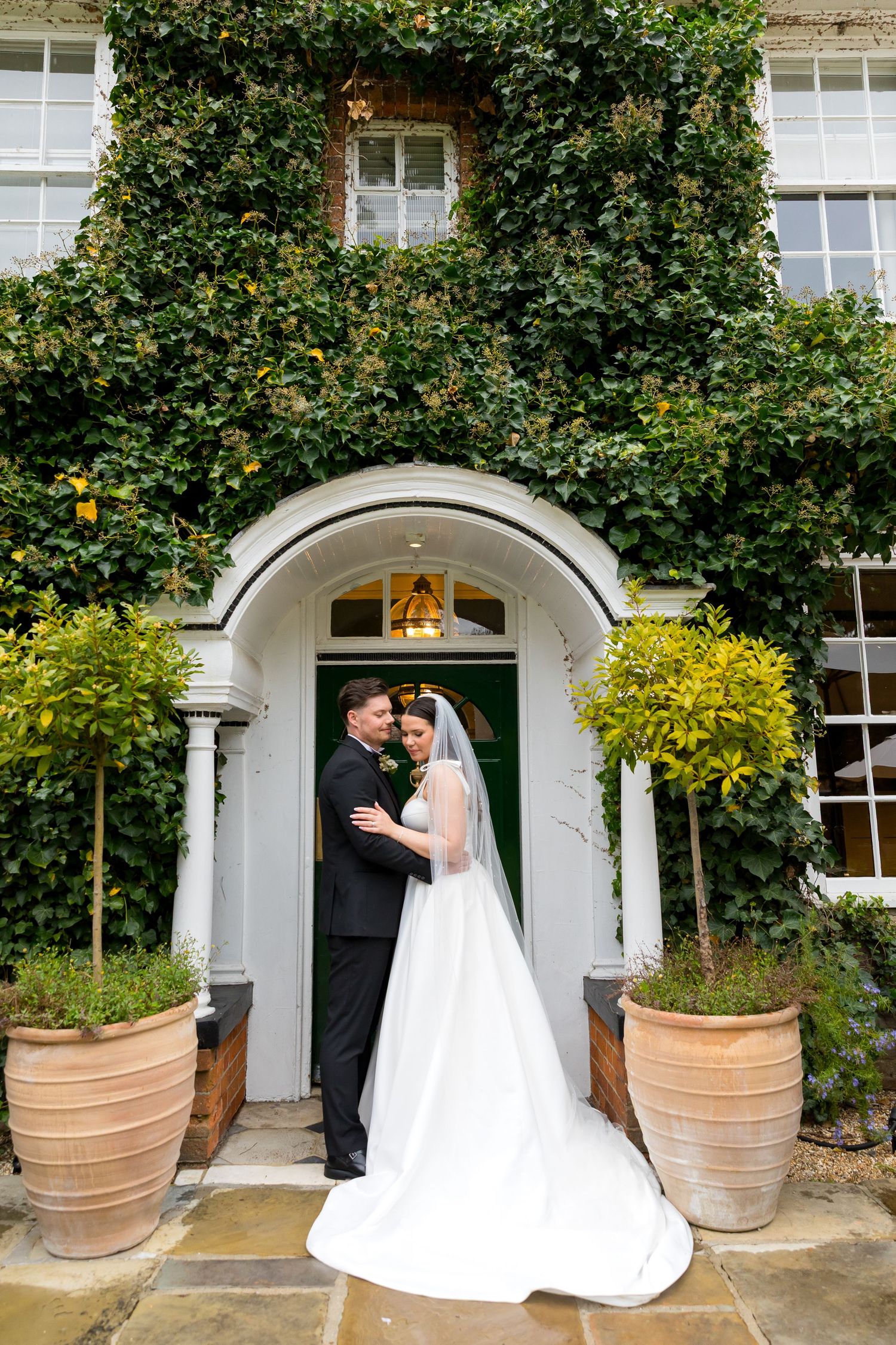 Bride and groom standing lovingly outside ivy-covered entrance at The Bush Hotel, Farnham on their wedding day.