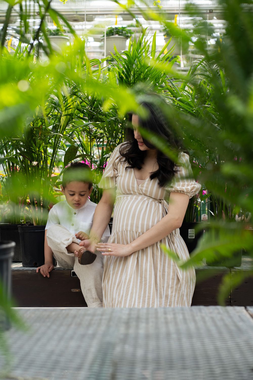 Pregnant women helping her toddler with the shoes in a greenhouse