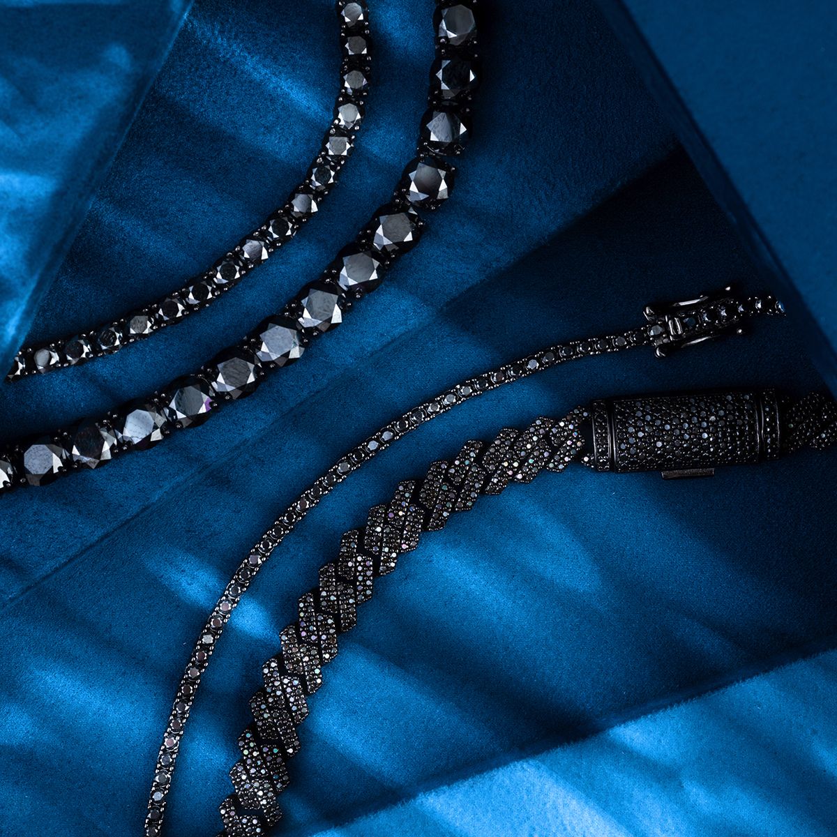 Close-up jewelry photography showing a layered pearl and chain necklace against blue fabric