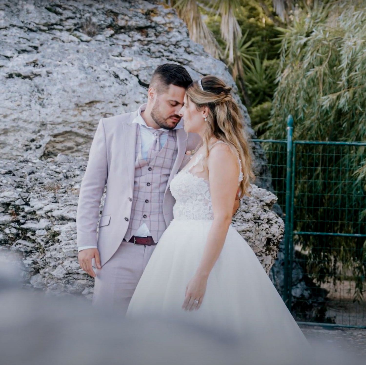 A couple shares an intimate moment in wedding attire against a rocky backdrop.