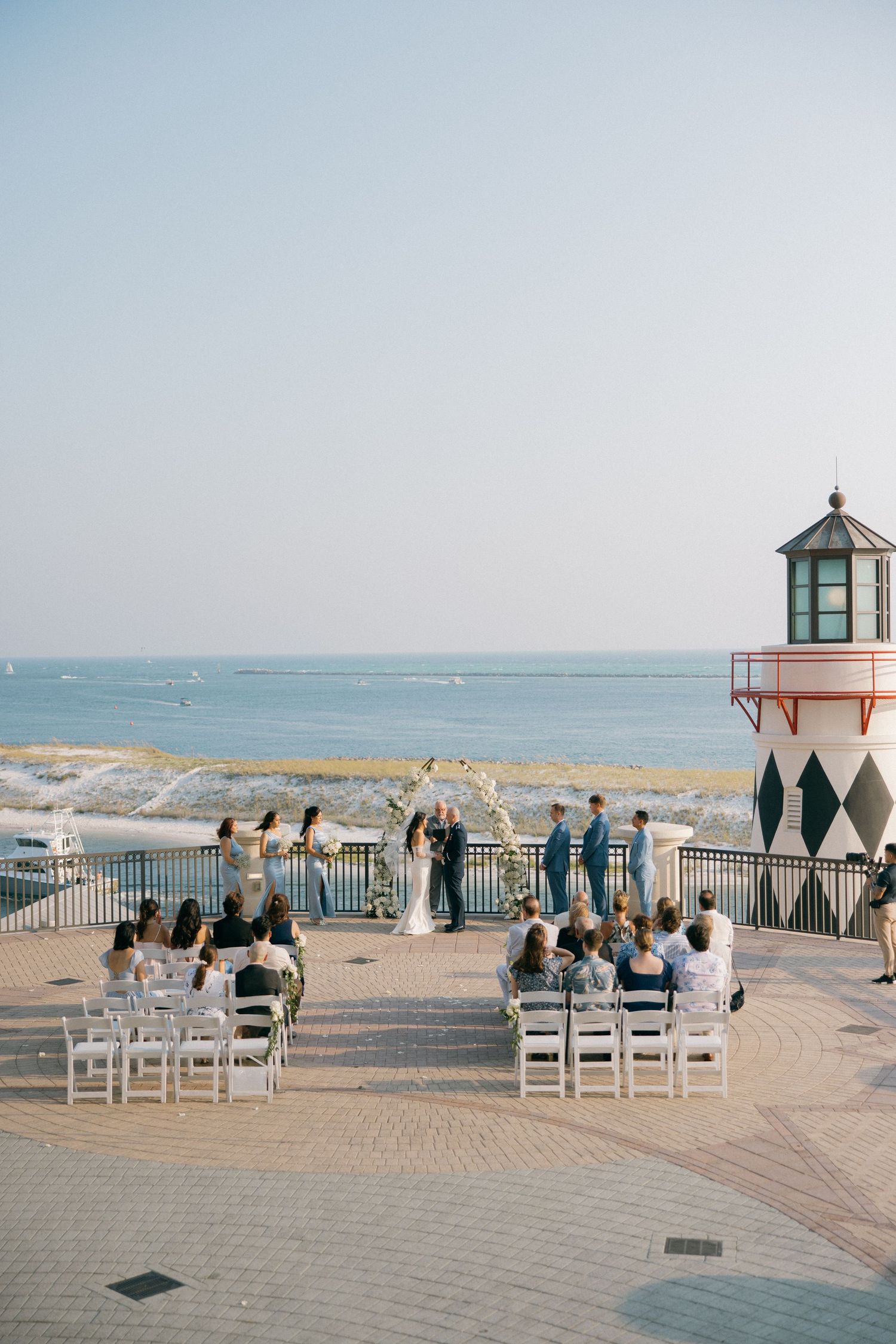 White chairs arranged for a beachside wedding ceremony with a lighthouse and ocean view in the background.