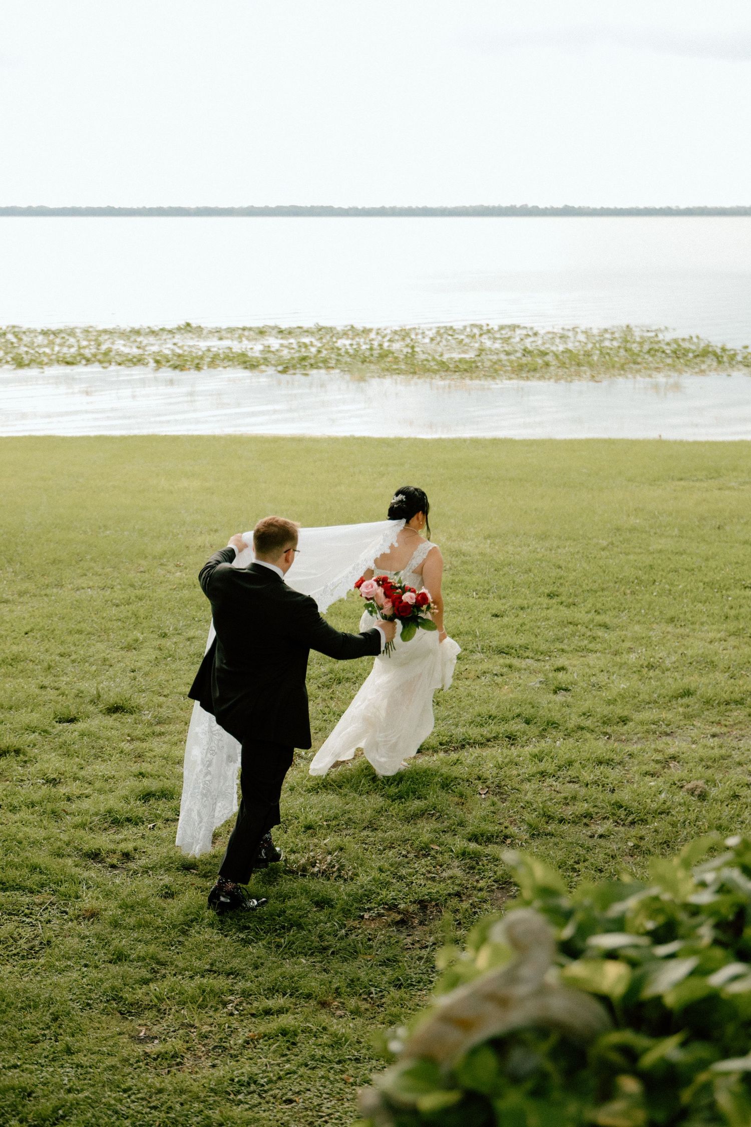 A couple dances together in a grassy field on their wedding day with flowing white dress and black suit.