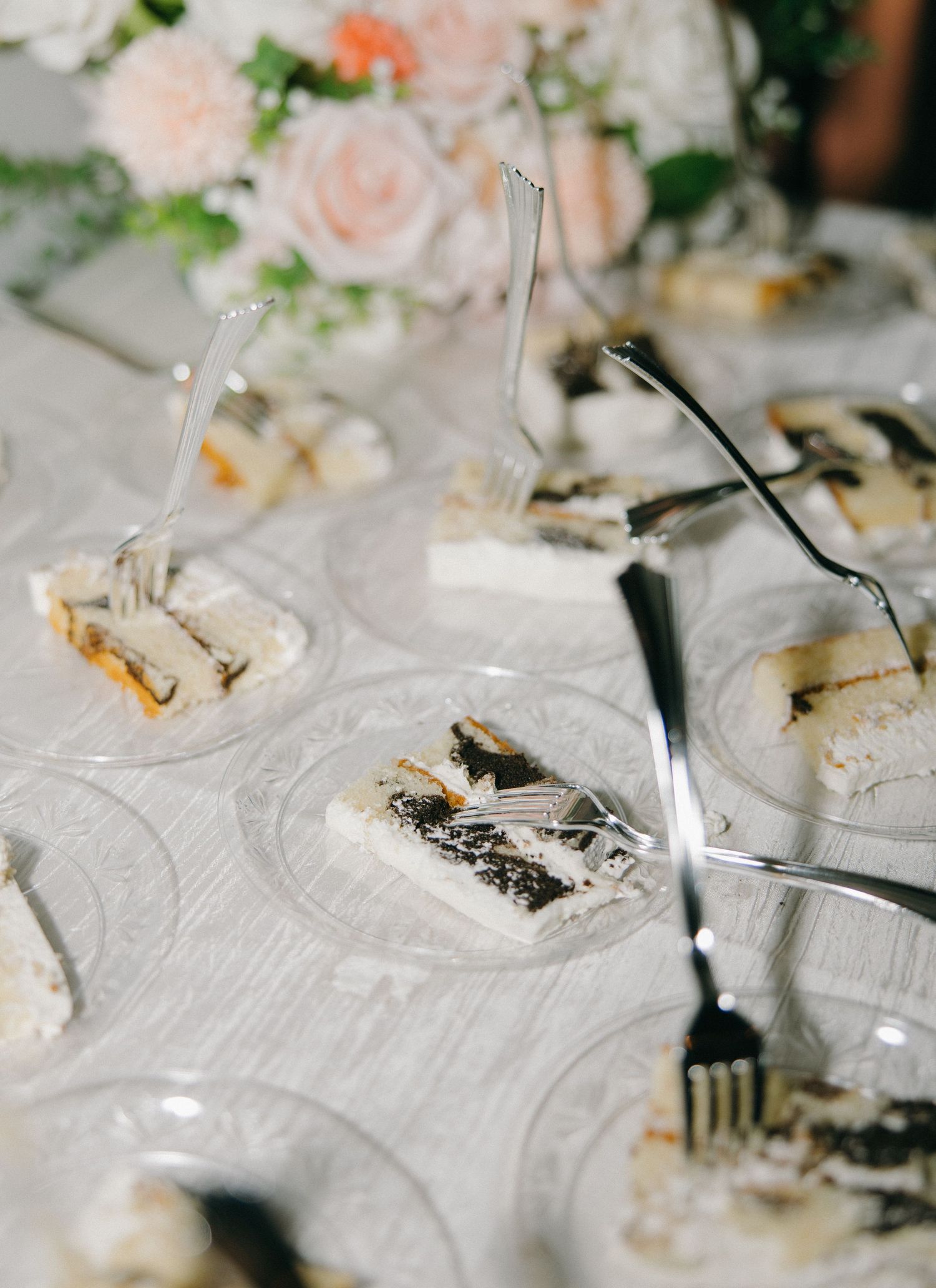 Close-up view of elegant wedding reception place settings with delicate plates and silverware on white tablecloths.