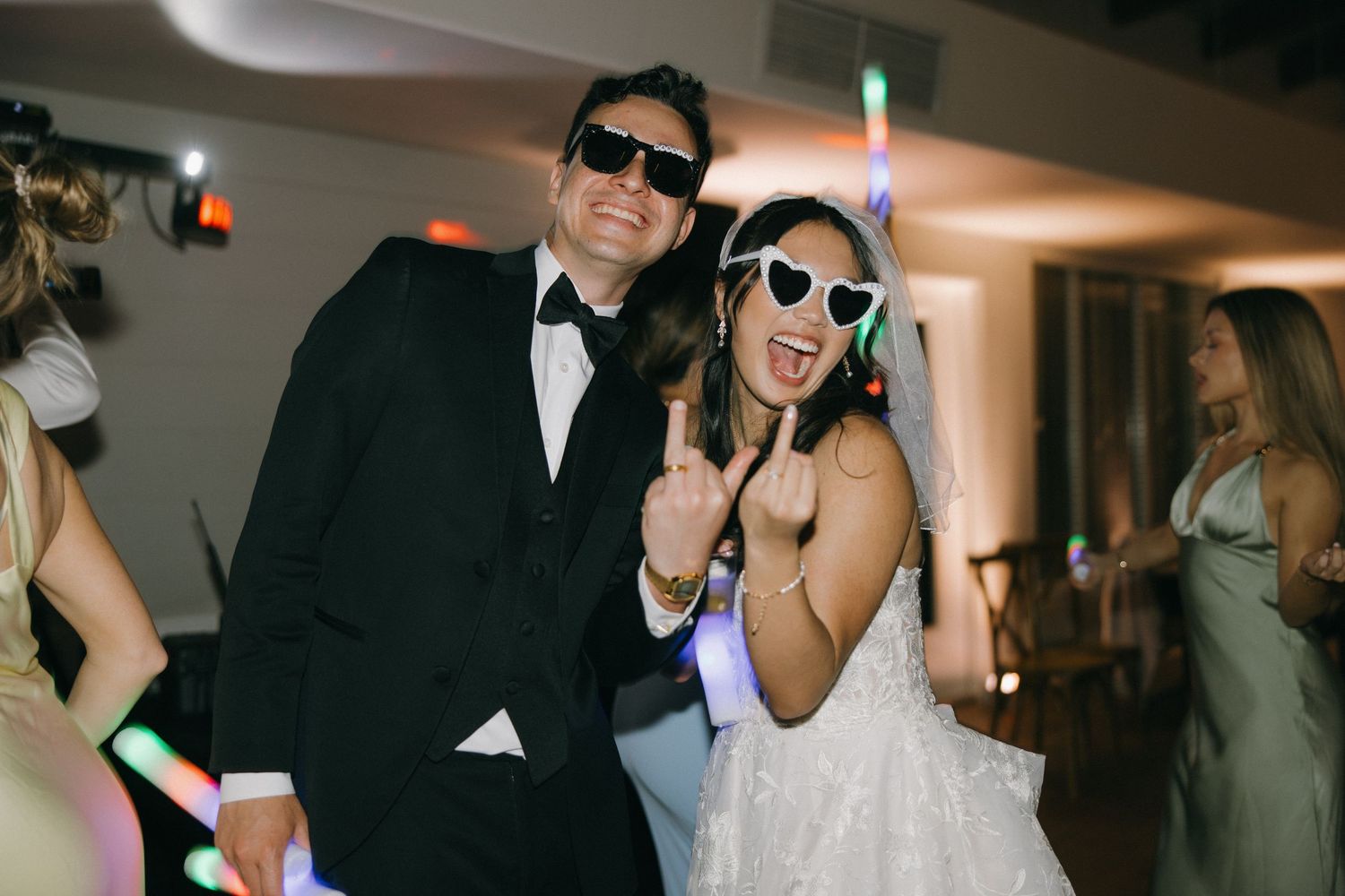 A bride and groom wearing matching sunglasses strike playful poses at their wedding reception.
