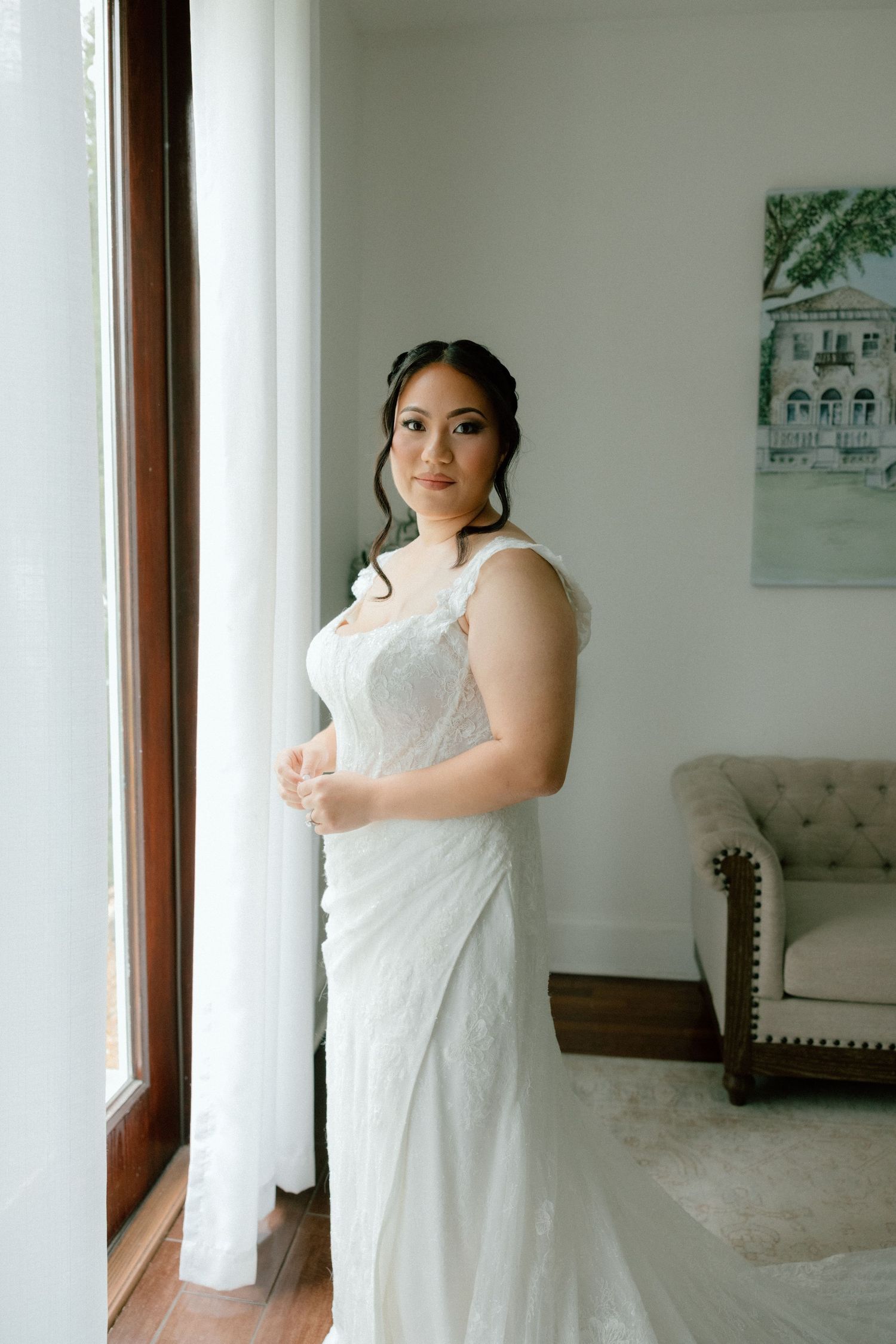 A person in a white sleeveless dress poses in front of windows in a bright, modern interior space.