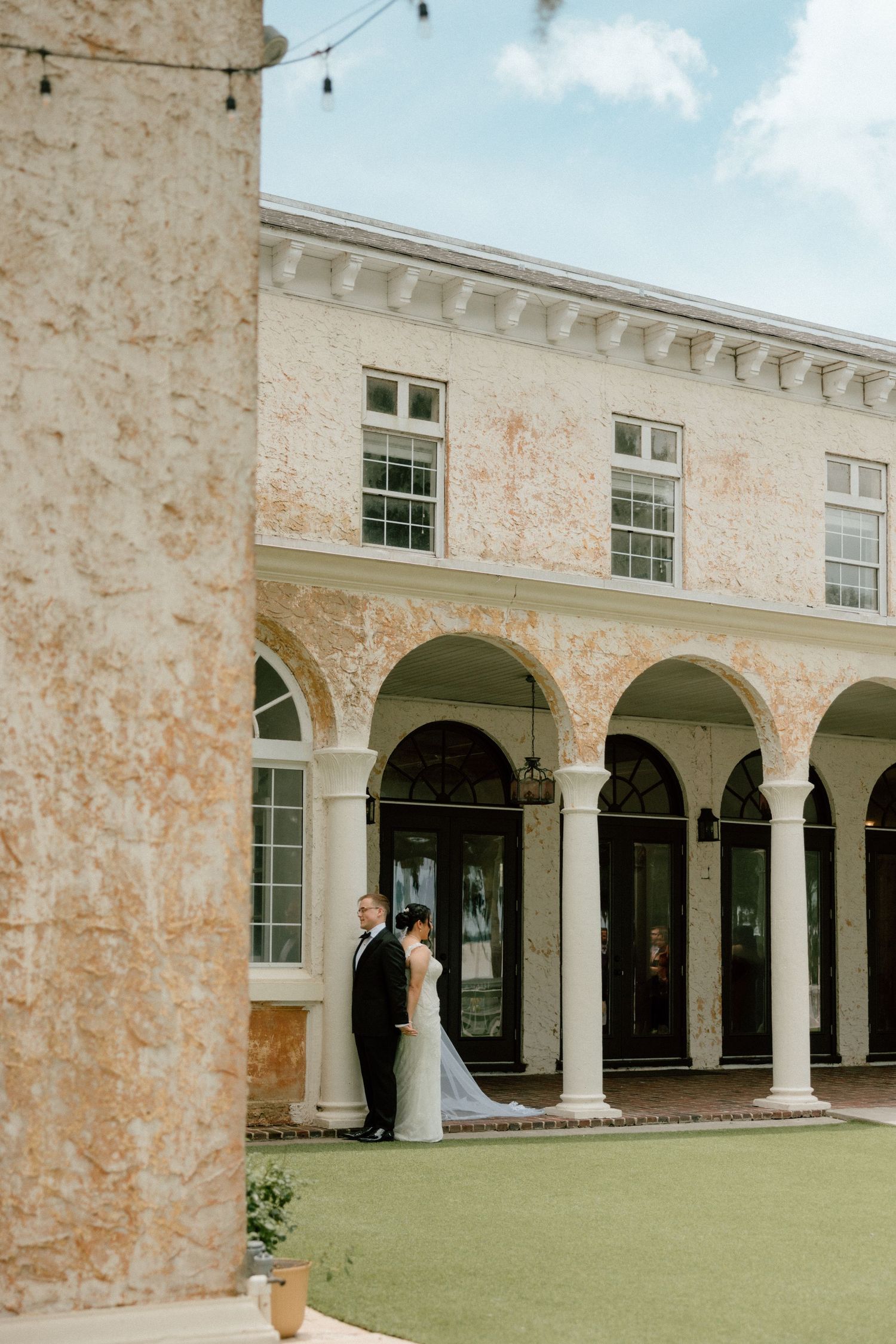 Elegant white stone colonnade with arched walkways surrounds a manicured lawn courtyard at a Italian stately venue.