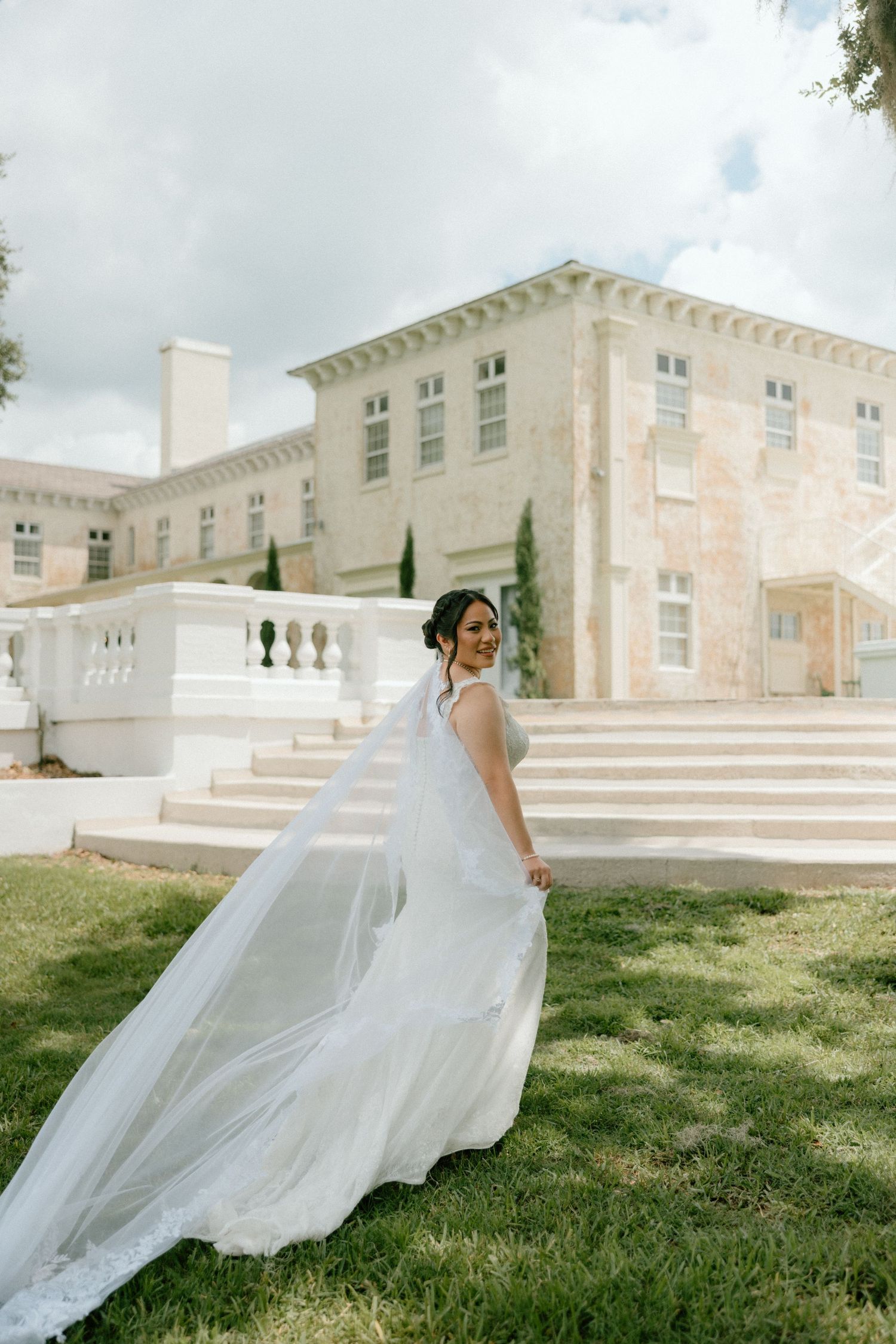 A flowing white wedding gown with long veil photographed against a grand Italian stone mansion.