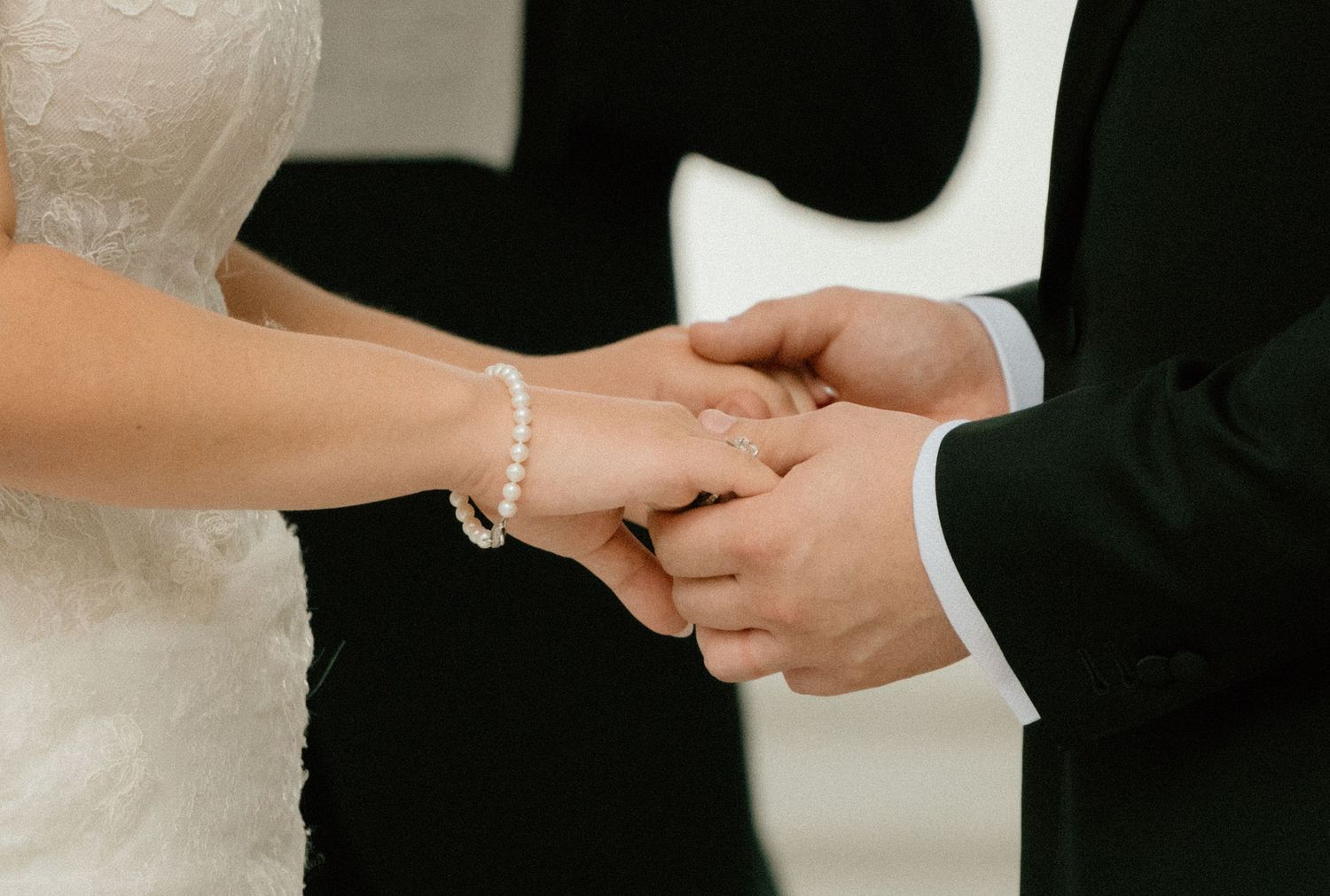 An intimate couple holds hands during a wedding ceremony while exchanging rings in a romantic moment.