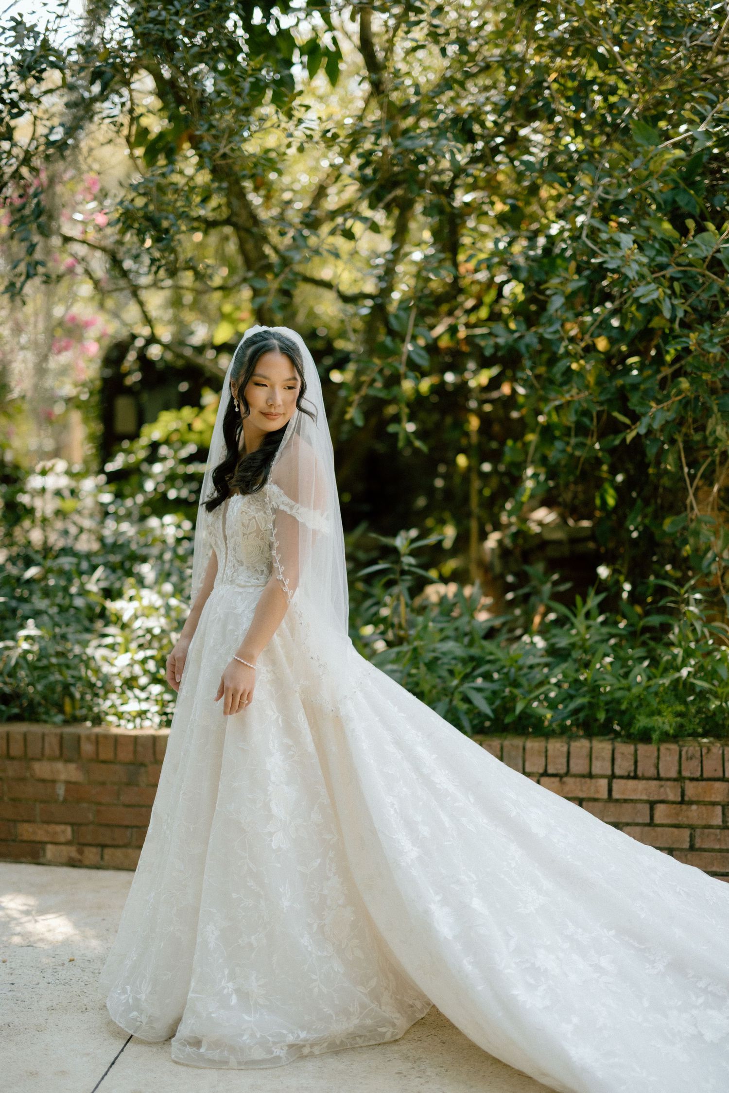 Bridal portrait is essential on your big day. Elegant white lace wedding dress with long train displayed in a garden setting.