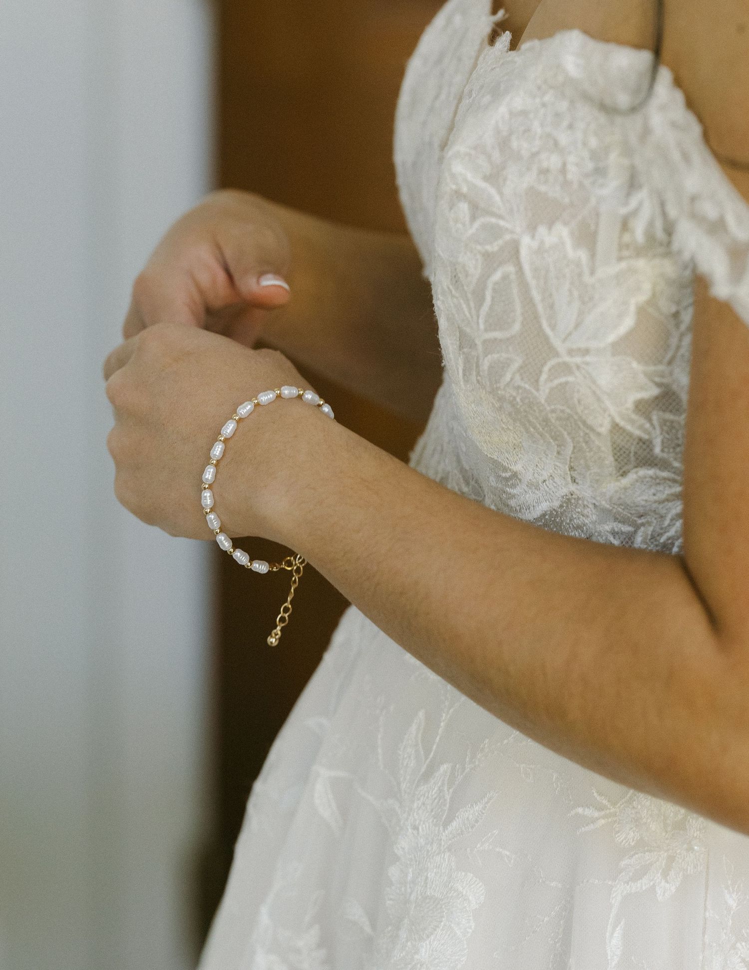 Close-up view of delicate lace details and pearl bracelet on an elegant white wedding dress sleeve.