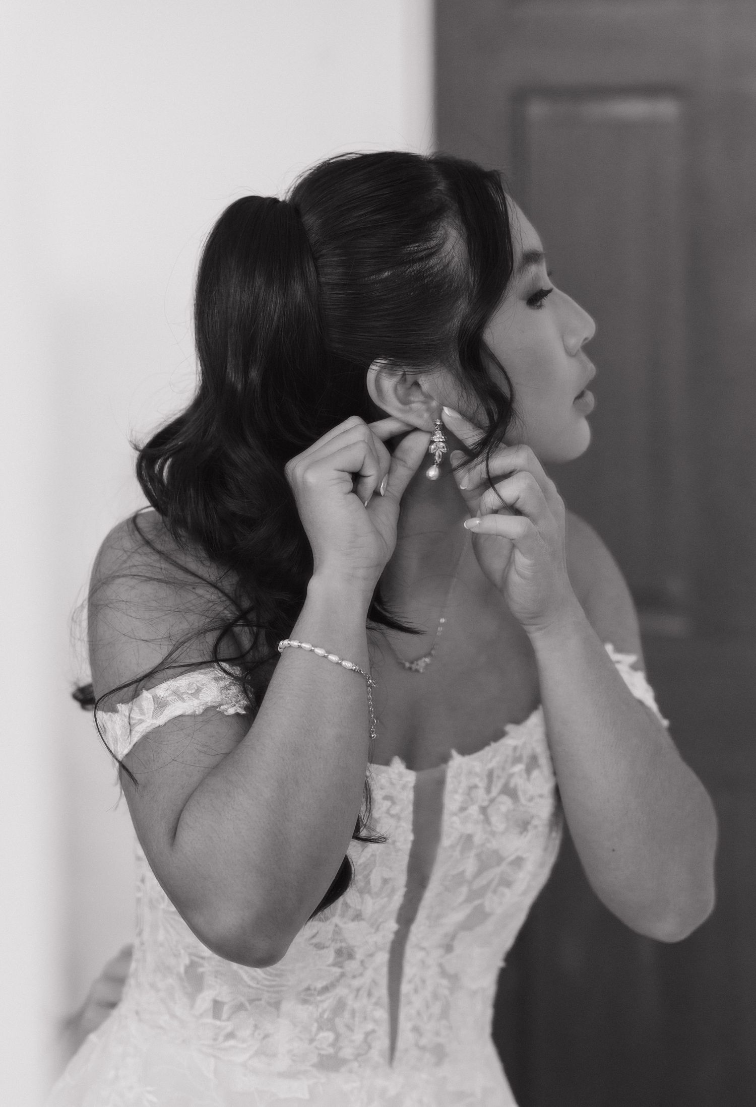 Black and white photo sequence shows bride putting on pearl earrings while getting ready for wedding ceremony.
